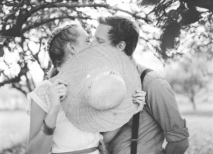 dreamy vintage engagement in an orchard kiss behind vintage straw hat camera color film fuji400h medium format vibrant