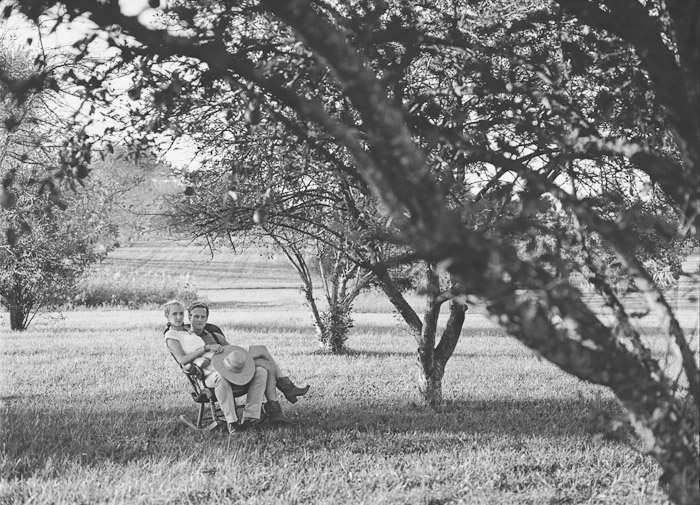 engaged couple sit together in an orchard in an antique chair film kodak tri-x