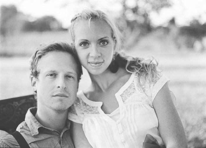 engaged couple sit together in an orchard in an antique chair film kodak tri-x