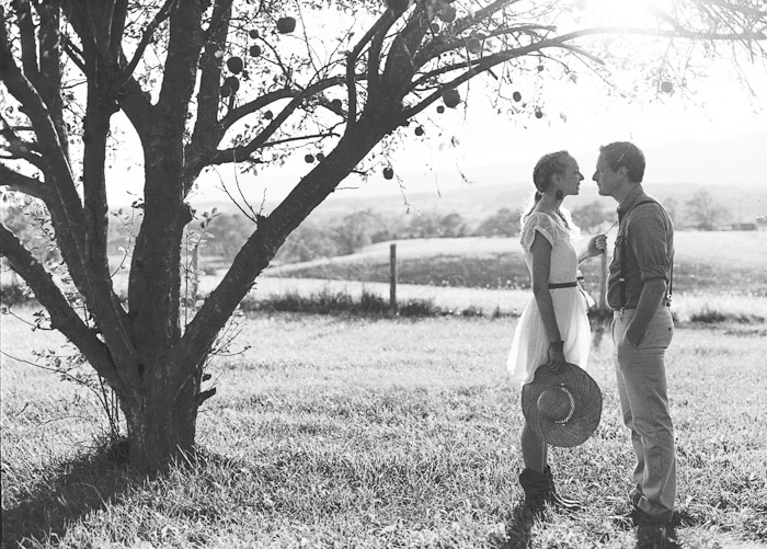 engaged couple sit together in an orchard in an antique chair film kodak tri-x