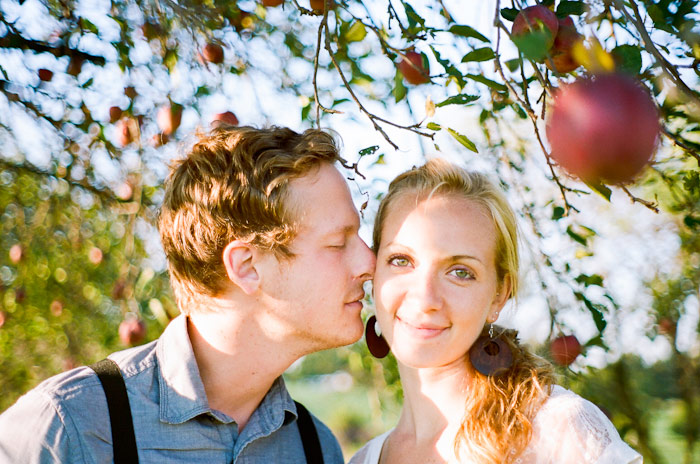 engaged couple sit together in an orchard in an antique chair film kodak tri-x