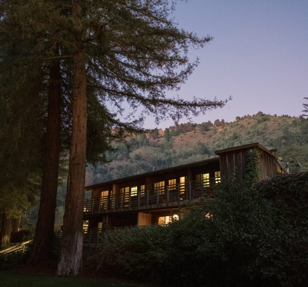color photograph of Big Sur River Inn at dusk with redwood trees and mountains in the background