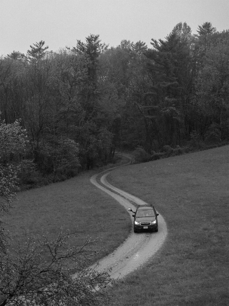 black and white photograph of bride and groom driving away from wedding at Haines chapel - bride sticking bouquet out of window